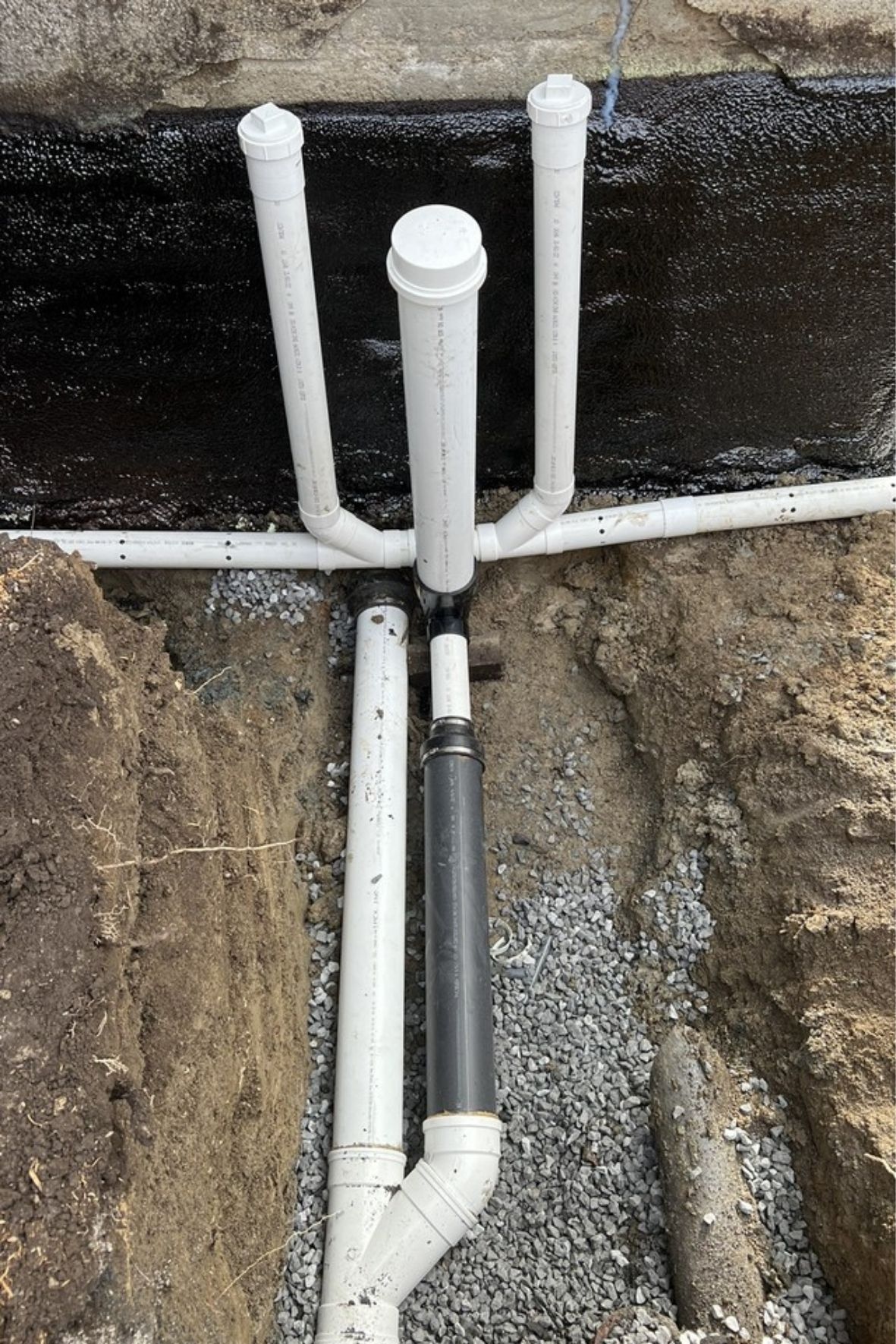 Tuyaux installés le long d’un mur de fondation avec revêtement noir et gravier au Québec